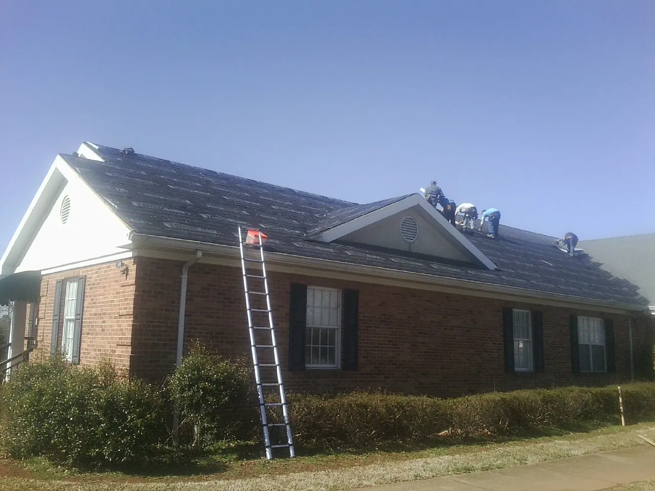 Crew tearing shingles off a brick ranch roof with a ladder set — Metal Roof Repair work by our crew in Perrysburg