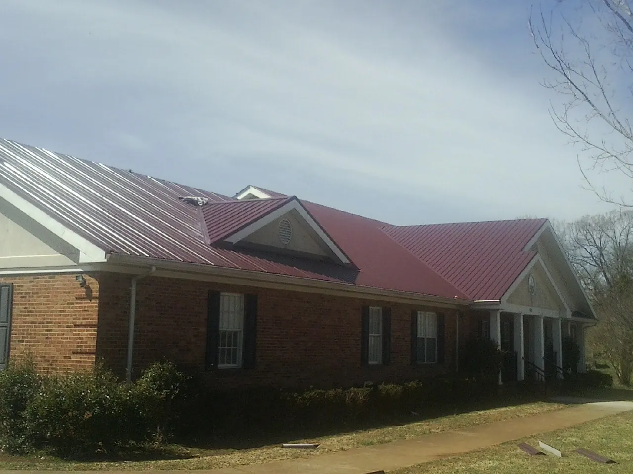 Red metal roof with gabled entries on a long brick building, from a Hail Damage Roof Repair job in Perrysburg