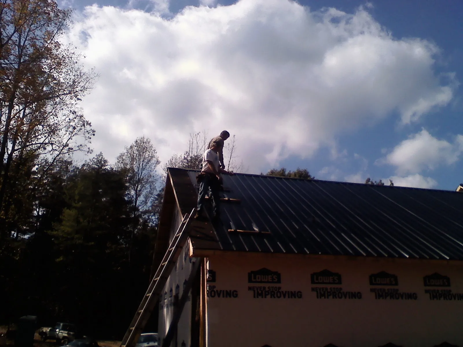 Roofer fastening dark metal panels high against a cloudy sky, from a Roof Inspection job in Perrysburg