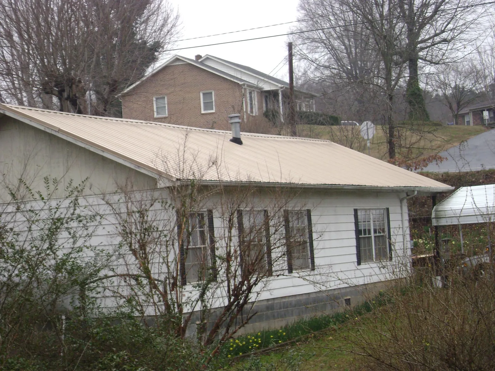 Tan metal roof on a white sided house set into a hillside — Commercial Roofing by Roofing Brothers in Perrysburg